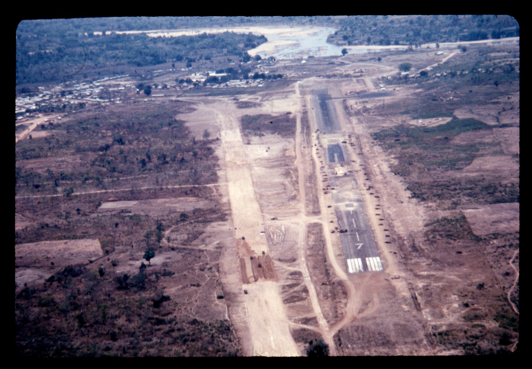 An aerial photograph of an airstrip under construction in a wide valley with hills beyond