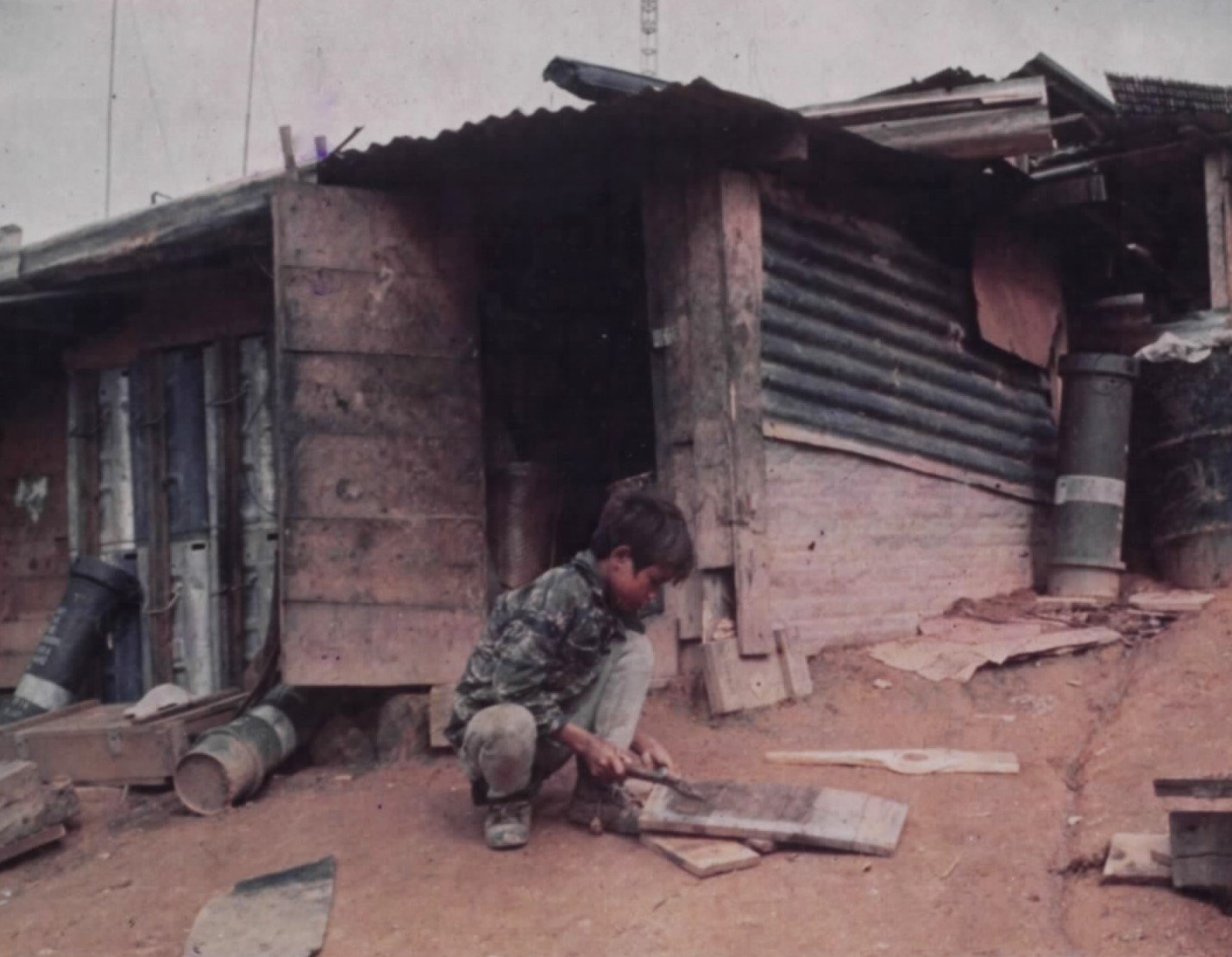 A boy repairing a small wooden house inside a military camp