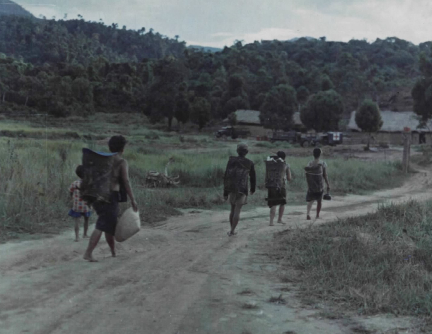 Villagers walking along a dirt road carrying loads, with hills behind