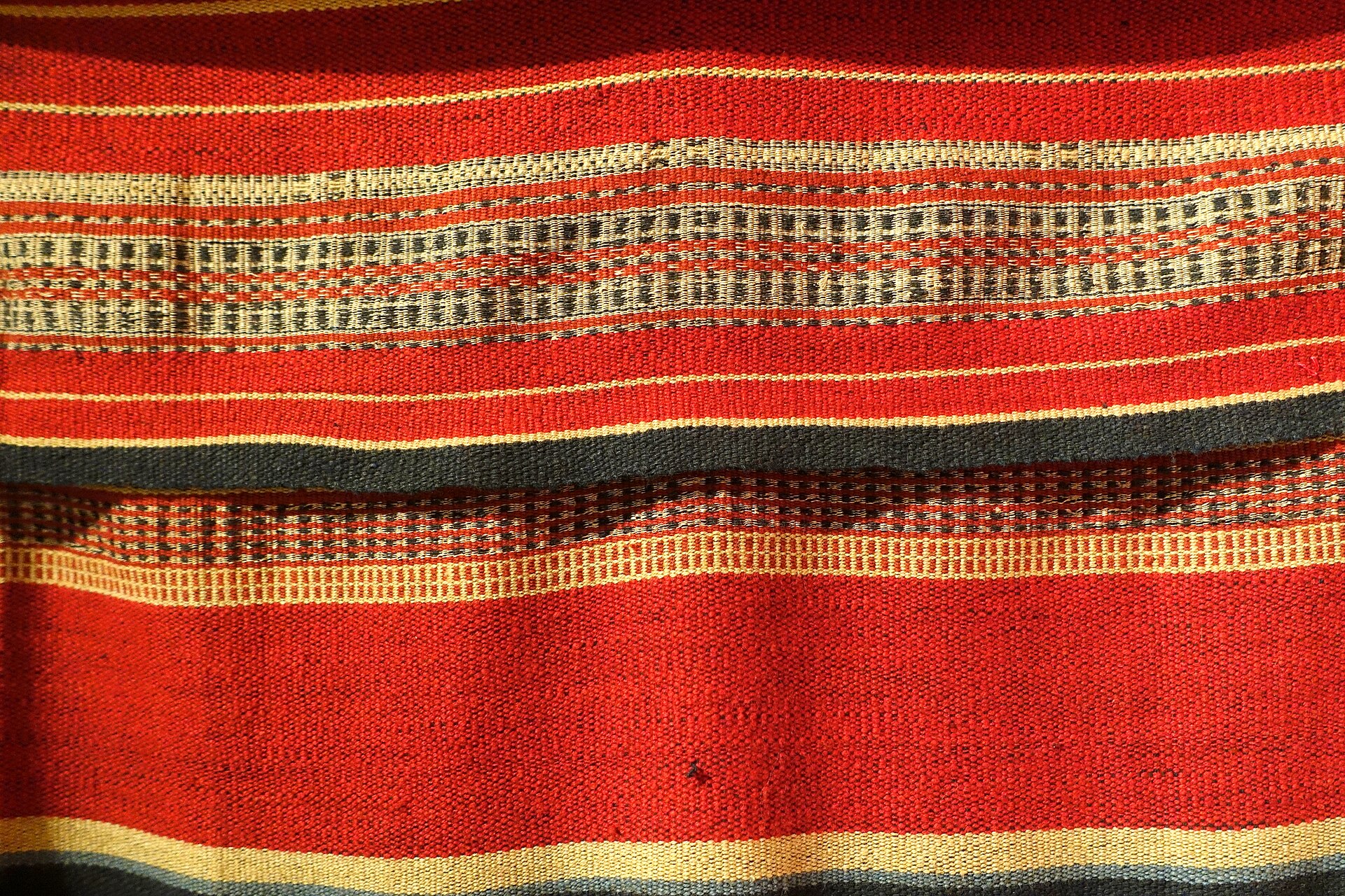 Detail of a handwoven cotton garment with red, black and white patterned bands