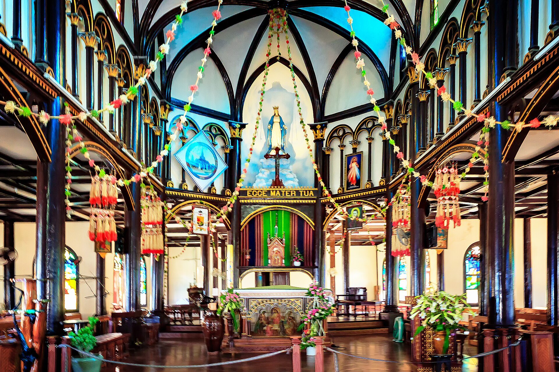 The interior of a wooden church, pale columns and pointed arches leading to a decorated altar